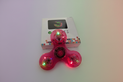 Pink fidget spinner with LED lights in front of its packaging box.