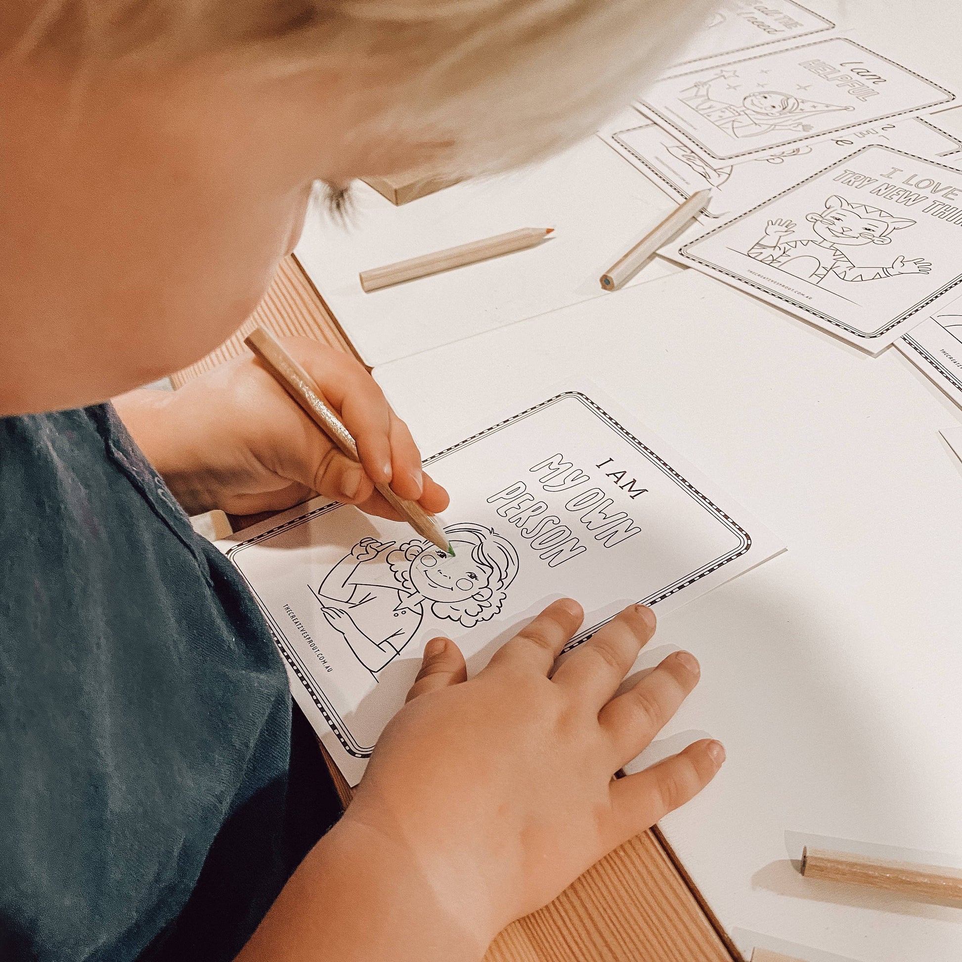 Child coloring a book with a pencil on a table with coloring pages.