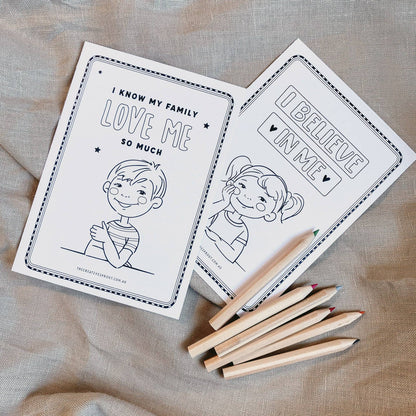 Two coloring books with illustrations and text on a textured fabric background, accompanied by wooden crayons.